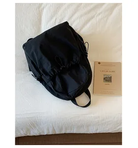 Minimalist black drawstring backpack with textured fabric shown next to a book on a bed