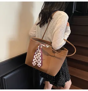 Detail view of a brown tote bag with a polka dot scarf tied to the handle on a model