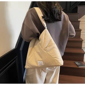 Detail of beige triangular canvas tote bag with KEEP GOING label on a wooden staircase