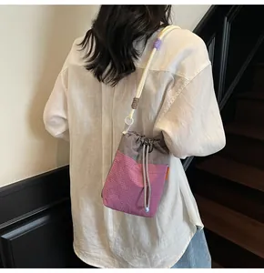 Detail of a drawstring bucket bag with purple check pattern and beaded rope shoulder strap