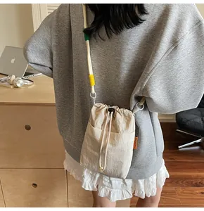 Close-up of beige nylon bucket bag with dual-color braided rope and side brand label