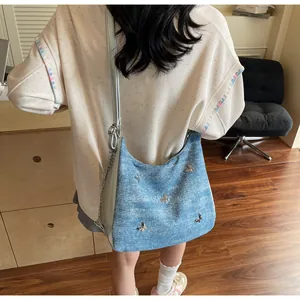 Détail d'un sac à épaule en denim bleu avec décorations papillons en métal et sangle à chaîne