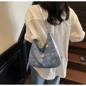 Détail du sac à épaule en jean bleu avec papillons 3D argentés et détails de chaîne