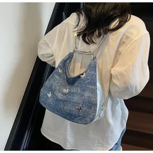 Détail du sac à épaule en denim bleu avec papillons argentés et bandoulière en chaîne