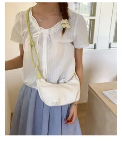 Detail shot of a cream crescent-shaped underarm bag with slim light green strap on shoulder