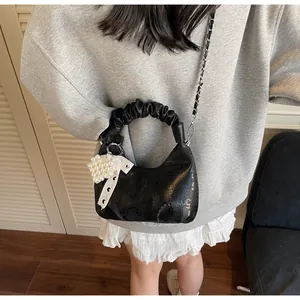 Detail of black pleated handbag with metal chain strap and pearl heart pendant