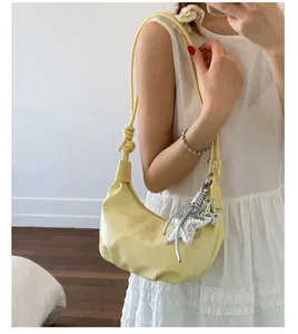 Detail of light yellow crescent hobo bag featuring knotted strap and star charm accessory
