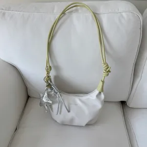 Detail of cream crescent shoulder bag with yellow strap and silver star charm pendant