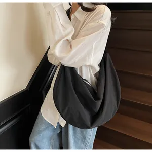 Model wearing a large black crescent crossbody bag with minimalist pleated fabric texture