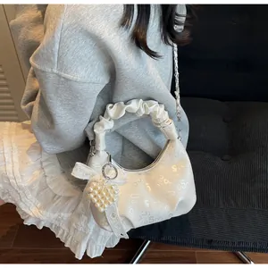 Close-up of white pleated handbag featuring pearl heart pendant and silver chain detail