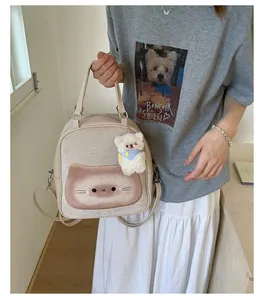 Detail of light beige tote backpack with brown cat face print and white bear plush charm