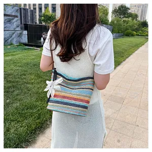 Detail of colorful striped straw bucket bag with floral charm and slim leather strap