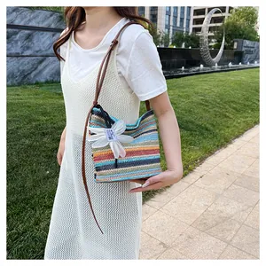 Close-up of rainbow striped straw bucket bag with white flower charm and brown strap