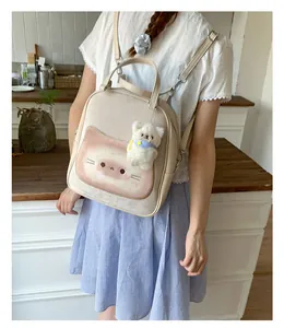 Detail of beige canvas backpack with pink cat face print and white plush bear charm