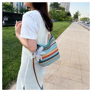 Detailed outdoor view of rainbow striped woven bucket bag with white flower charm and strap