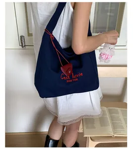 Detail of navy canvas tote bag featuring red C'est la vie embroidery and leather charm