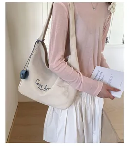 Detail of a large cream canvas tote bag with blue lettering and a small navy round charm