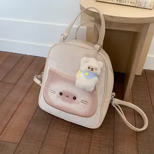 Beige cartoon cat backpack with plush bear charm on a warm wooden floor setting