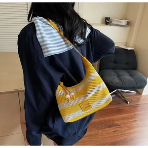 Détail d'un sac tissé à rayures jaunes et blanches avec logo en cuir et perles décoratives