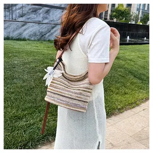 Detail of a rainbow striped woven bag featuring a white flower charm and slim brown strap