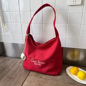 Large red canvas tote bag with C'est la vie embroidery on a rustic wooden table