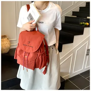 Detalle de mochila de lona naranja con bordado 'take it easy' en la solapa de apertura