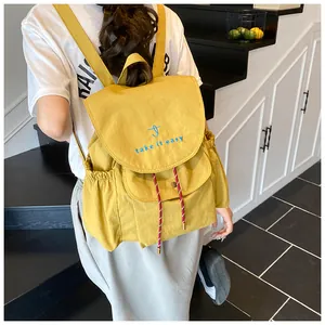 Detalle de mochila de nailon amarillo con bordado y cordones rojos y blancos trenzados