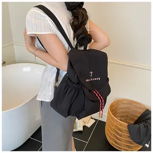 Vista detallada de la mochila de lona negra con bordado rosa y cordón a rayas laterales