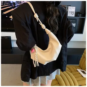 Sac demi-lune beige avec nœud et breloque cœur porté à l'épaule par un mannequin