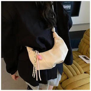 Détail du sac croissant blanc cassé avec poignée nouée et breloque gland cœur