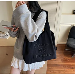 Dettaglio della borsa tote nera con testo Chase My Dreams a rilievo su tessuto opaco