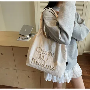 Dettaglio del ricamo 'Chase My Dreams' su una grande borsa tote in tela beige a spalla