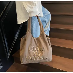 Dettaglio della borsa tote taupe con ricamo mostrata su una scala in legno