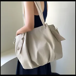 Detail of beige drawstring tote bag with decorative ribbons on a model's shoulder