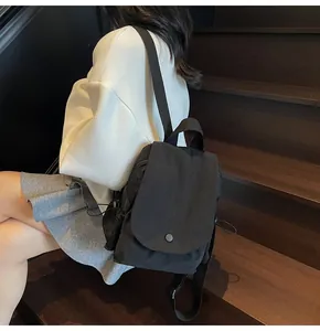 Detail view of a compact black nylon backpack with a stylish flap and side drawstring details