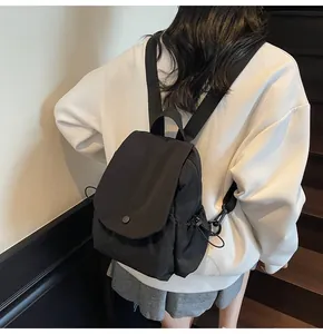 Detail of black nylon backpack with flap closure and side drawstring pockets on model