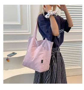 Close-up of light pink nylon tote bag with a front pocket and black woven brand label