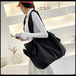 Large black canvas tote bag with shoulder strap and side bow detail on female model