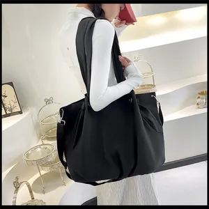 Detail of a large black nylon tote bag with pleated design worn by a model