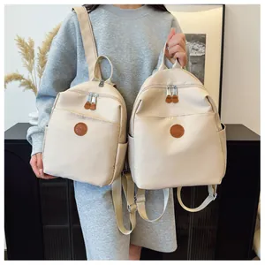Detail of beige nylon backpacks in two sizes with metal zippers and leather logo patch