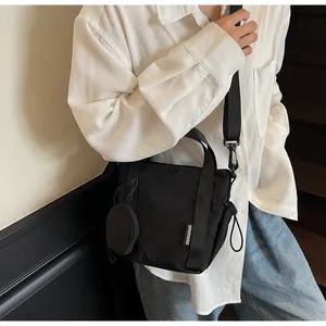 Detail of black nylon crossbody bag with mini round coin purse and white woven logo label