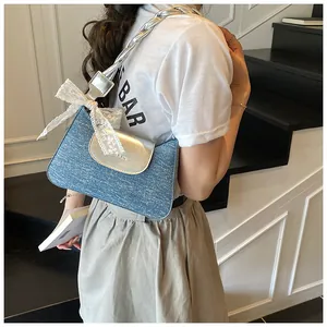 Blue denim underarm bag with silver flap and white lace bow detail shown on shoulder