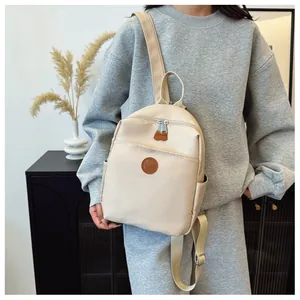 Detail of a beige nylon backpack featuring a leather logo patch and front zipper pocket