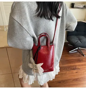 Detail view of red mini bucket bag with leather texture and white flower charm accessory