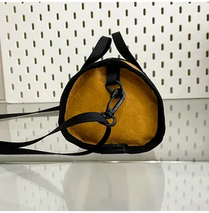 Detail of orange cylinder bag featuring textured fabric and black nylon handle strap
