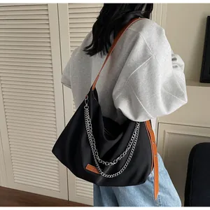 Detail of black nylon tote bag with silver chains and brown leather shoulder strap