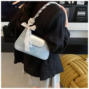 Detail of blue denim shoulder bag featuring silver metallic flap and white lace bow