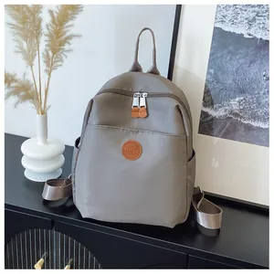 Close-up of dark grey nylon backpack featuring leather logo patch and dual zipper pockets