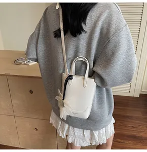 Detail of white bucket bag with floral charm and leather strap on a grey sweatshirt