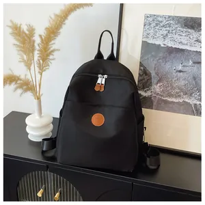 Detail of black nylon backpack featuring brown leather logo badge and silver metal zippers